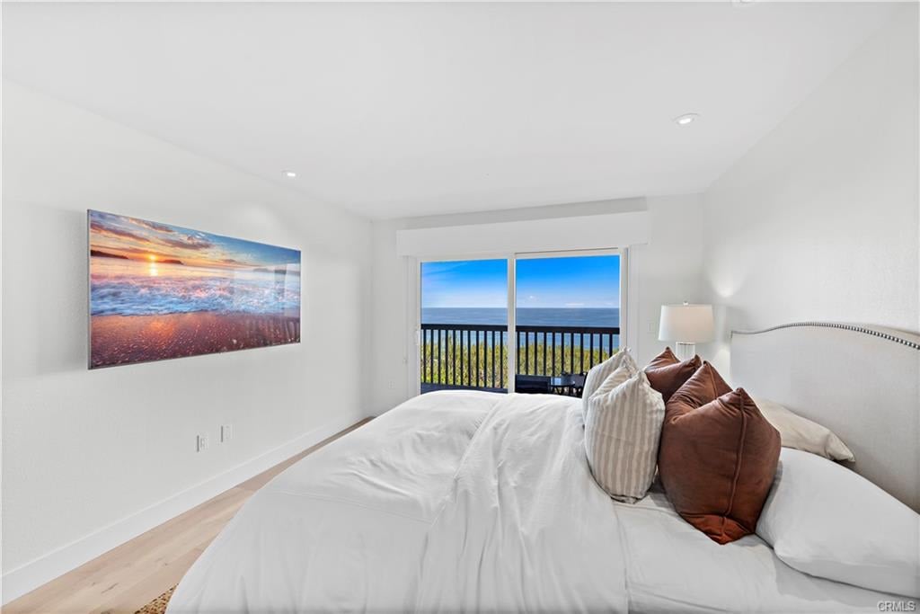 Furnished bedroom with a white bed, rust-colored pillows, and ocean views through sliding glass doors.