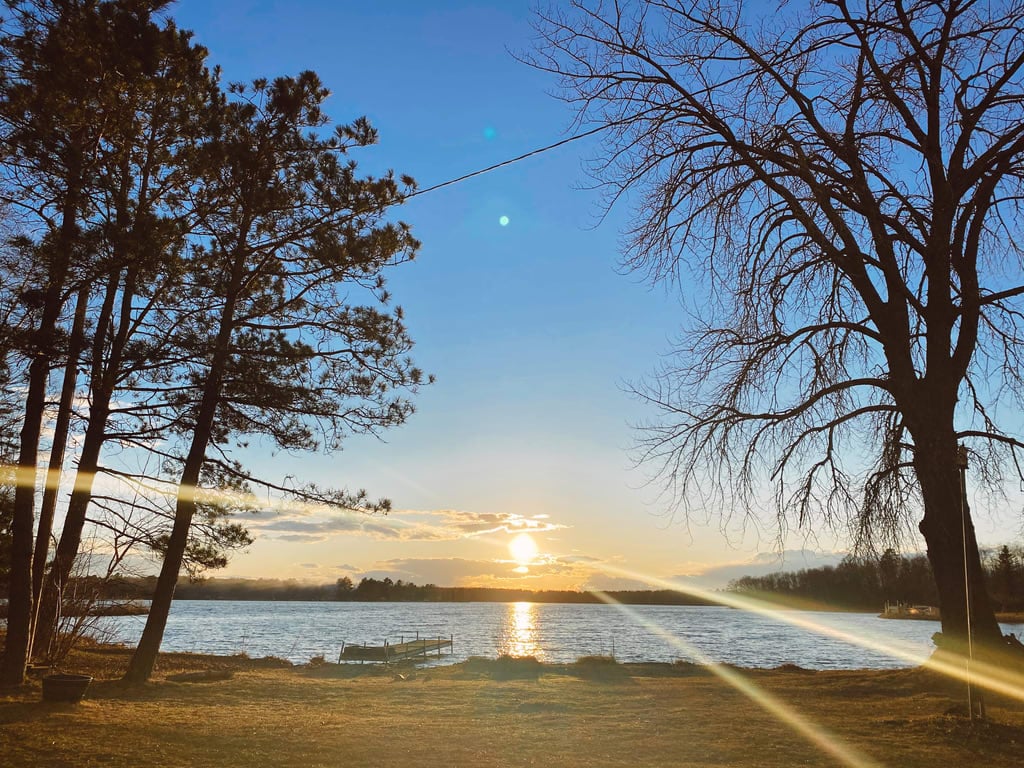 Tranquil lake under a serene sunset. The sky painted in orange, pink, and purple hues is mirrored in the calm waters.