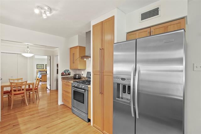 Kitchen with wood cabinetry, stainless steel appliances, hardwood floors, and a dining area beyond.