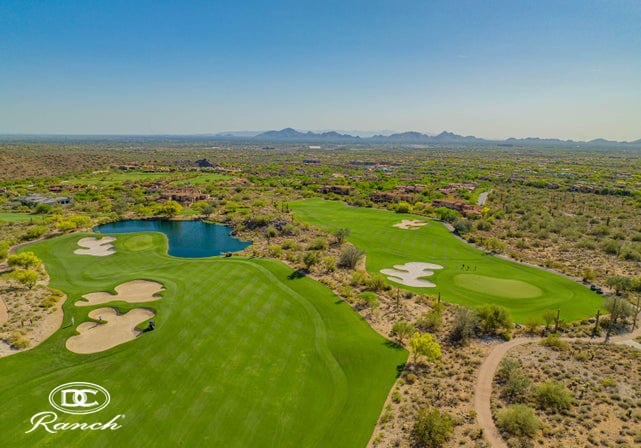 An aerial view of a golf course in the desert with ranches at the back