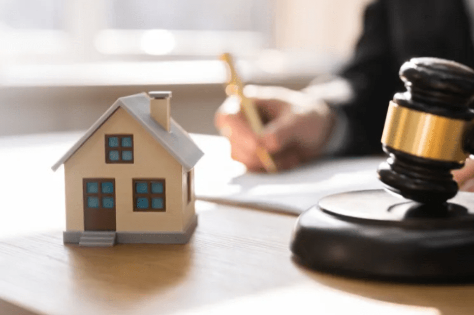 A model house beside a judge's gavel as someone writes at a desk.