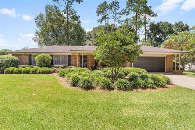 A single-story house in 3926 Tralee with a large, well-manicured front yard featuring various shrubs and trees. The house has a light-colored exterior and a welcoming entrance.