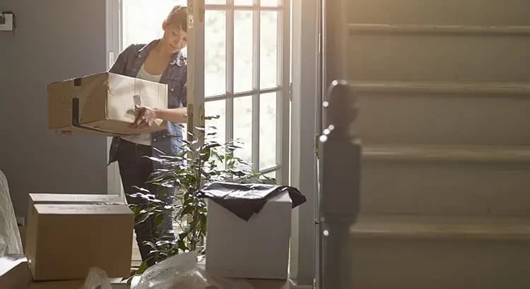 A person carrying a box and walking up a staircase, likely moving into a new home. The image is backlit, creating a warm, welcoming atmosphere.