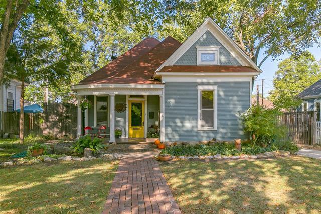 Blue-gray house with a yellow front door, red-brown roof, and brick walkway beneath mature trees.