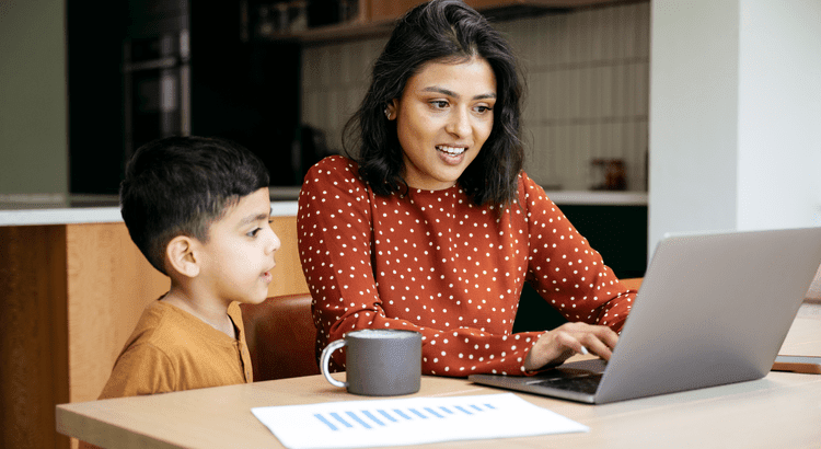 A woman using a laptop with a child looking at it beside her