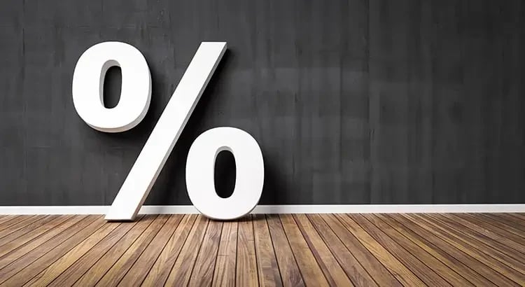 A large percentage symbol (%) on a wooden floor with a dark background, representing financial concepts such as interest rates or discounts.