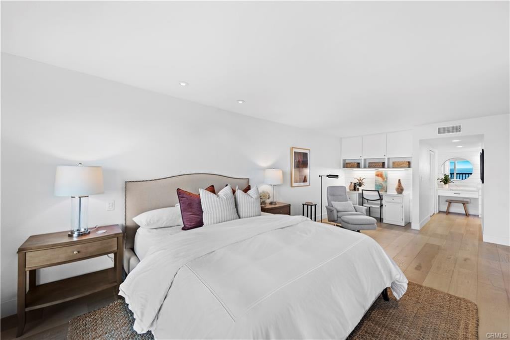 Staged bedroom with a large white bed, gray sitting chair, and light wood floors.