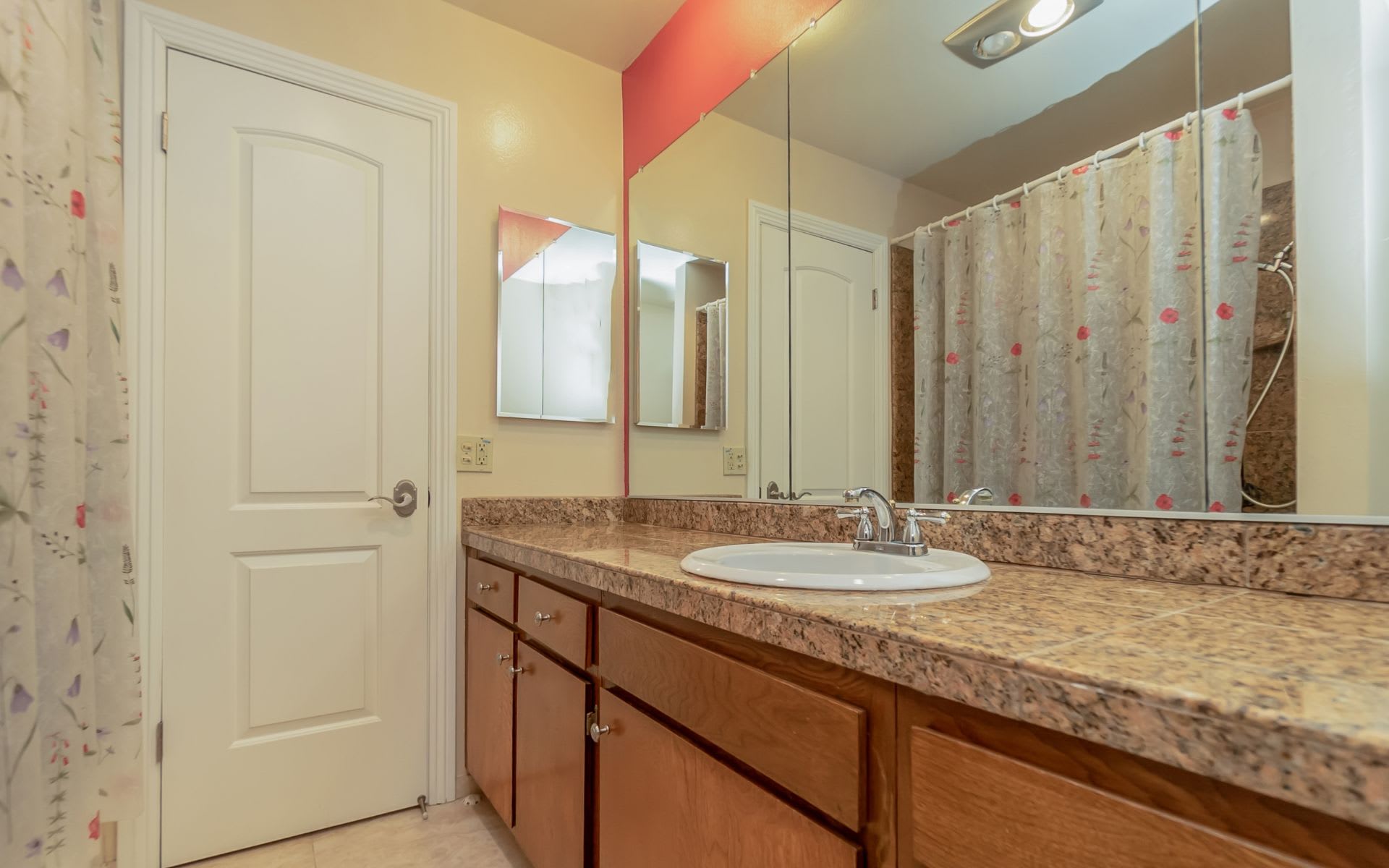 Bathroom with a long stone-look vanity, oval sink, mirrored wall, and floral shower curtain.