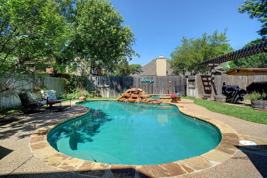 Backyard swimming pool with a rock waterfall, stone coping, and shaded patio seating.