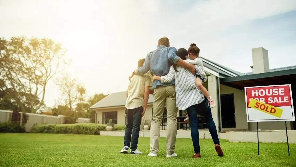 House with a sold sign as a family embraces on the front lawn.