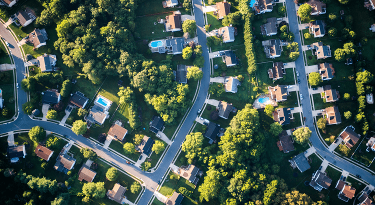 Aerial view showcasing a suburban residential neighborhood with houses, green lawns, and tree-lined streets.