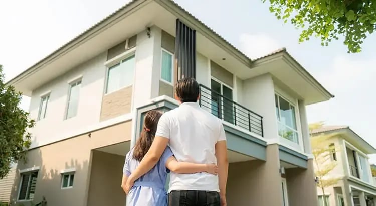 A couple embracing and looking at a modern house. The scene suggests they are considering buying the home or have recently moved in, symbolizing new beginnings or home ownership.