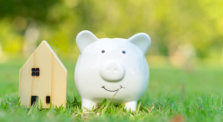A piggy bank and a small house model on a grassy background. This image represents financial savings and investment in real estate.