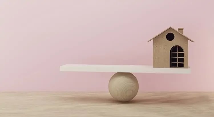 A small birdhouse on top of a minimalist, modern piece of furniture with a spherical leg. The background is a soft pink, creating a whimsical and artistic feel.