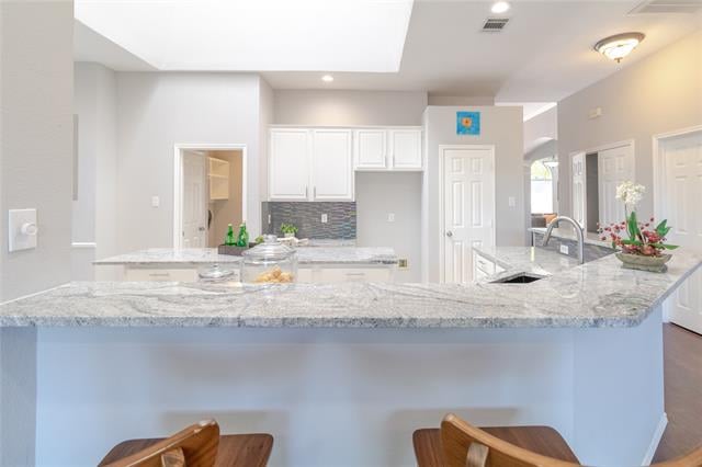 Kitchen with a large granite island, built-in sink, white cabinets, and gray tile backsplash.