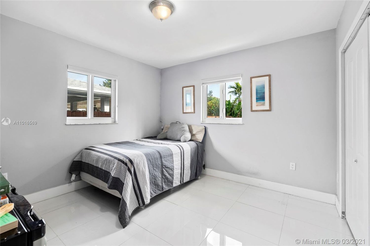 Bedroom with a gray-and-white striped bedspread, two windows, and glossy white tile flooring.