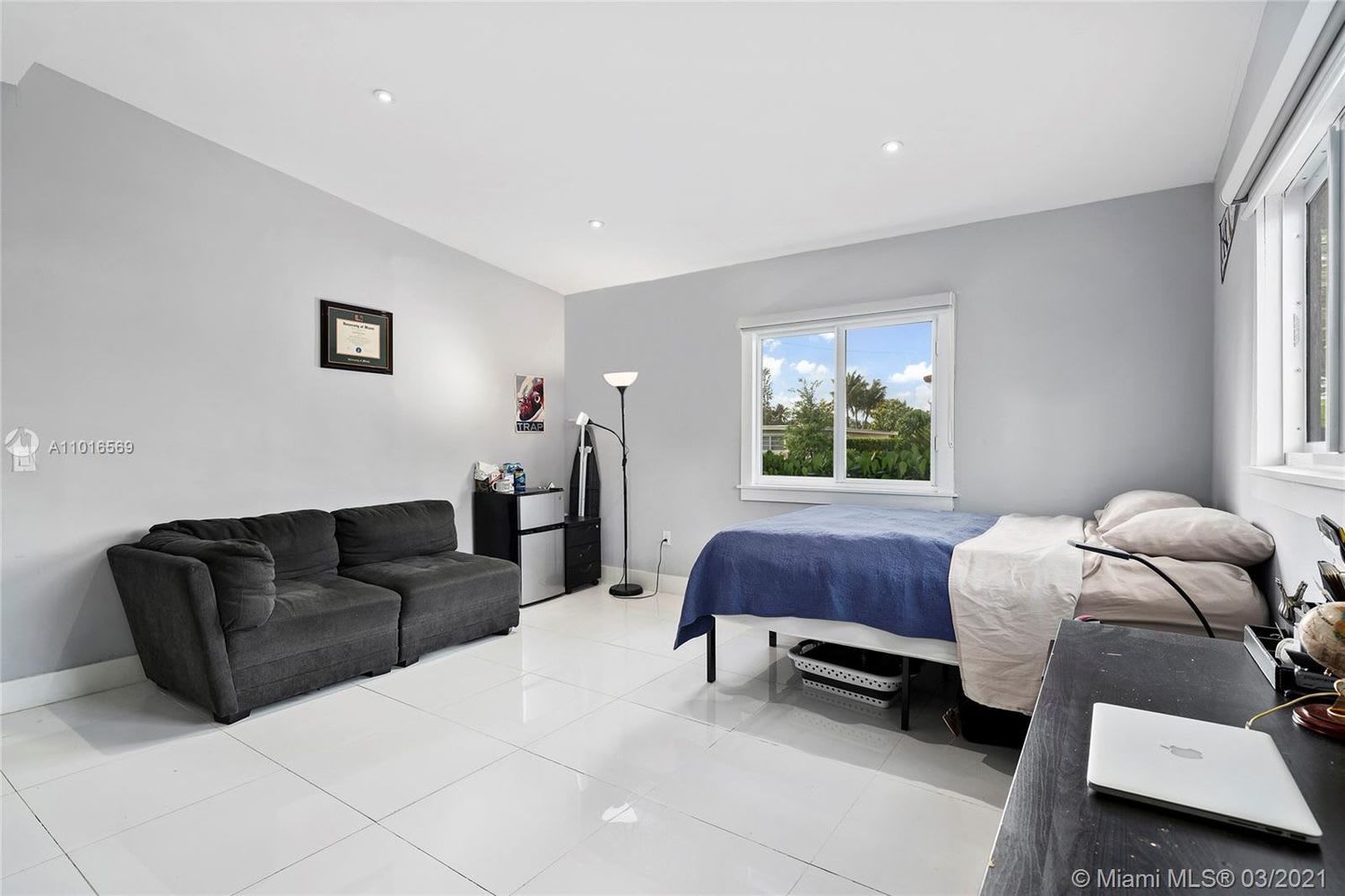 Bedroom with a blue-covered bed, dark gray sofa, and desk beside the windows.