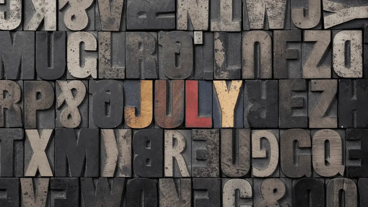 A collection of wooden letterpress type blocks forming the word "JULY" in red. This image represents the month of July, possibly highlighting events, holidays, or themes related to this month.