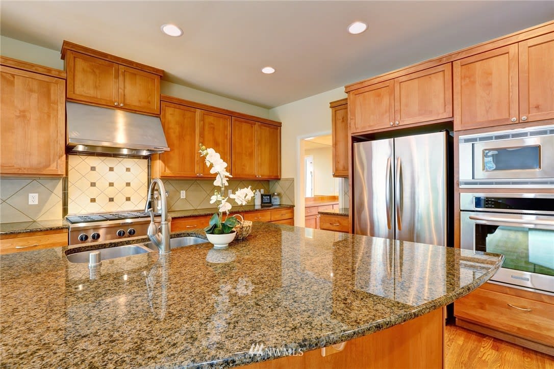 Kitchen with a broad granite island, warm wood cabinets, and stainless steel appliances.