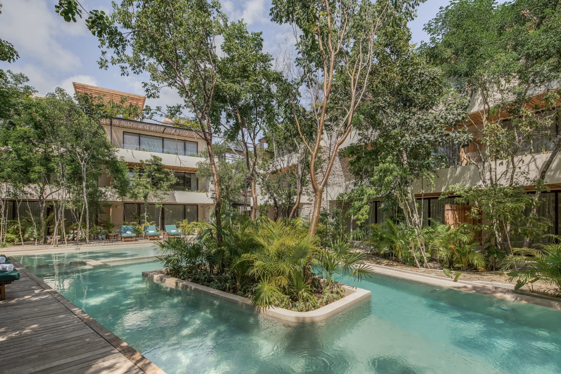 Condo-hotel pool surrounded by tropical landscaping, with modern buildings and balconies beyond.