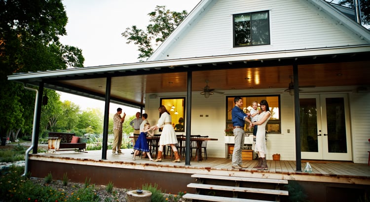 A photo of a family standing on the porch of a house, with a large porch and trees in the background.