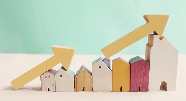 A set of small house models with upward-pointing arrows on a light blue background, symbolizing growth in real estate or housing market trends.