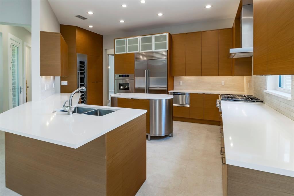 Modern kitchen with warm wood cabinets, white island, and stainless steel appliances.