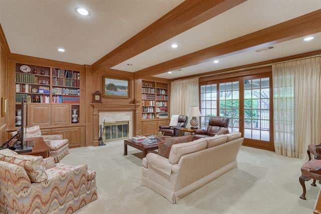 Living room with wood-paneled bookshelves, a fireplace, ceiling beams, and glass doors.