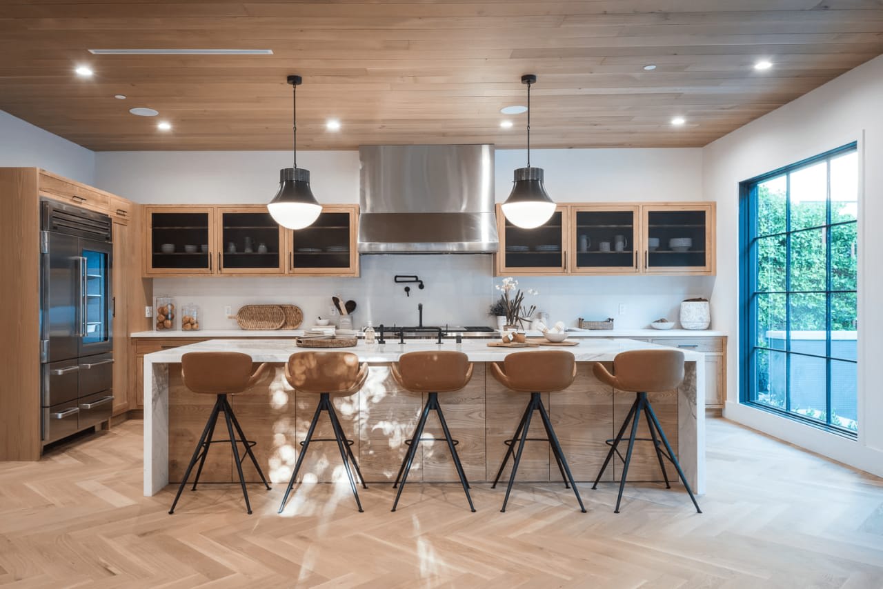 A photo of a modern kitchen with custom cabinetry, stainless steel appliances, and a large island with seating.