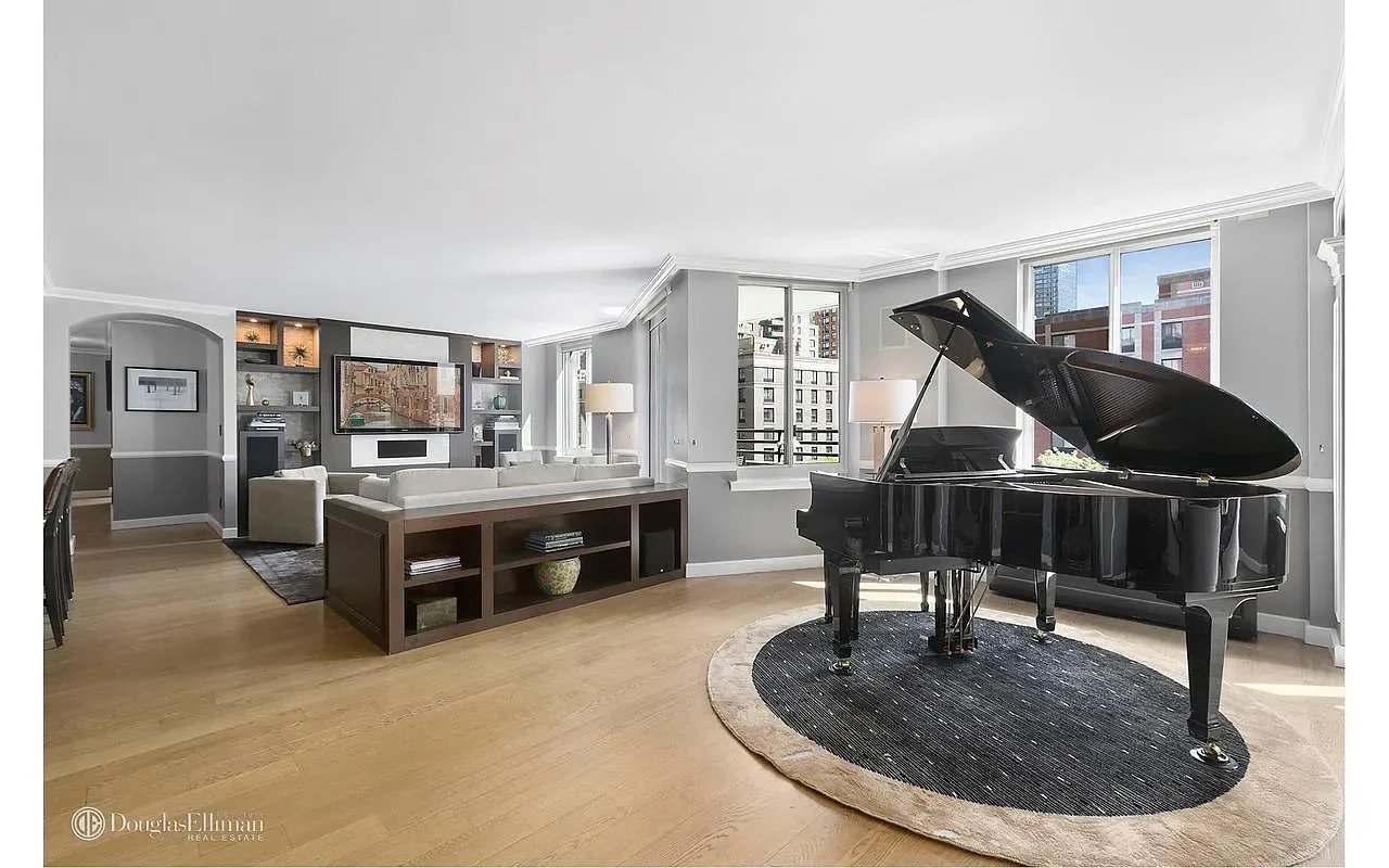 Furnished living room with a black grand piano, built-in shelving, and city views through large windows.
