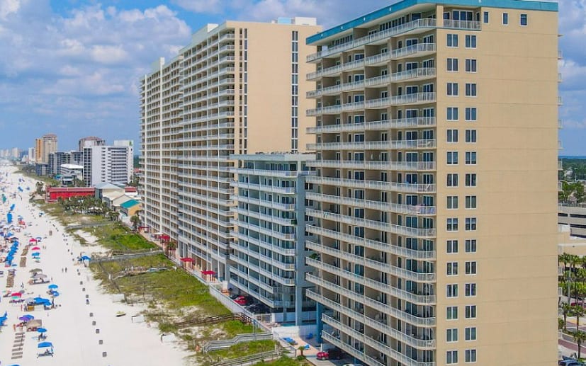 A row of tall, beige-colored high-rise buildings located directly on a sandy beach.