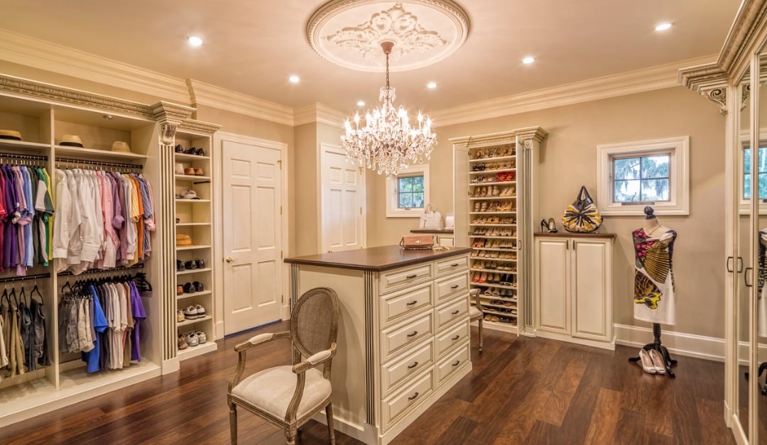 Walk-in closet with a central drawer island, shoe shelves, and a crystal chandelier.