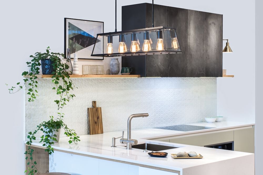 Modern kitchen with white counters, dark cabinets, and a long glass pendant light.