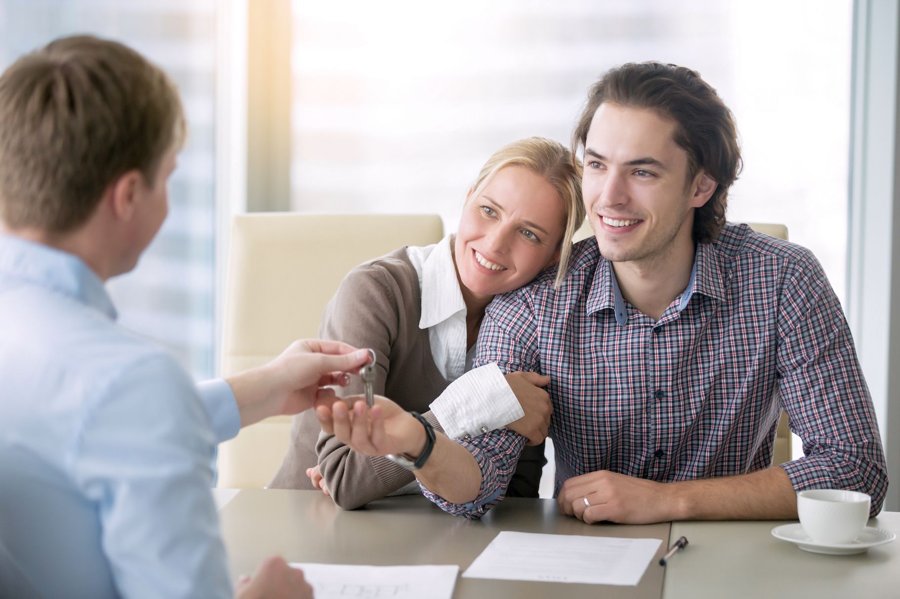A smiling couple receives house keys across a table with paperwork.