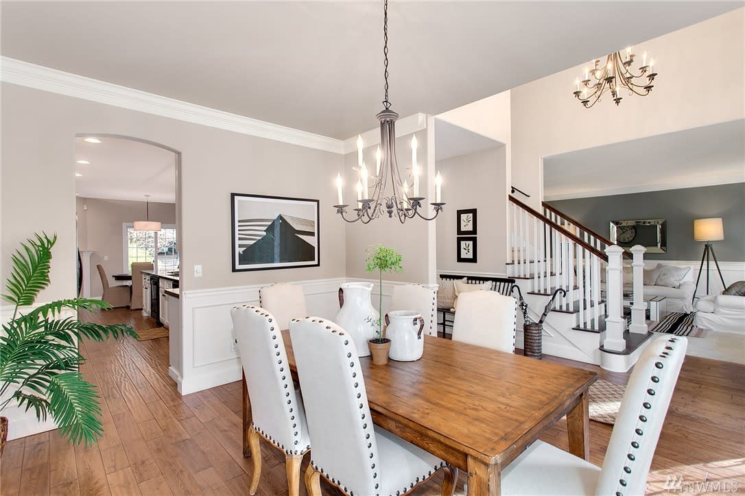 Dining room with a wooden table, white chairs, hardwood floors, and a chandelier.