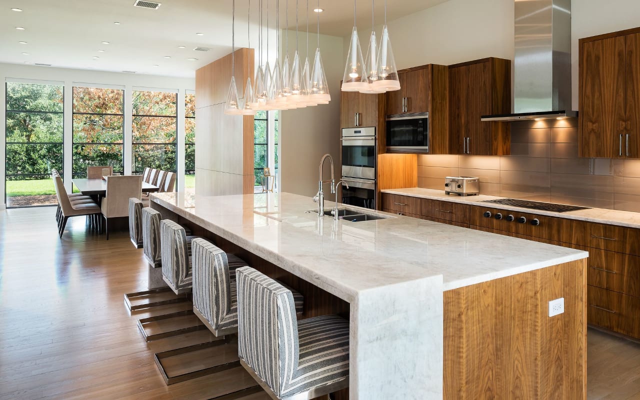 Captivating kitchen with dark cabinets, chandeliers, and a breakfast nook, combining elegance and natural light in style.