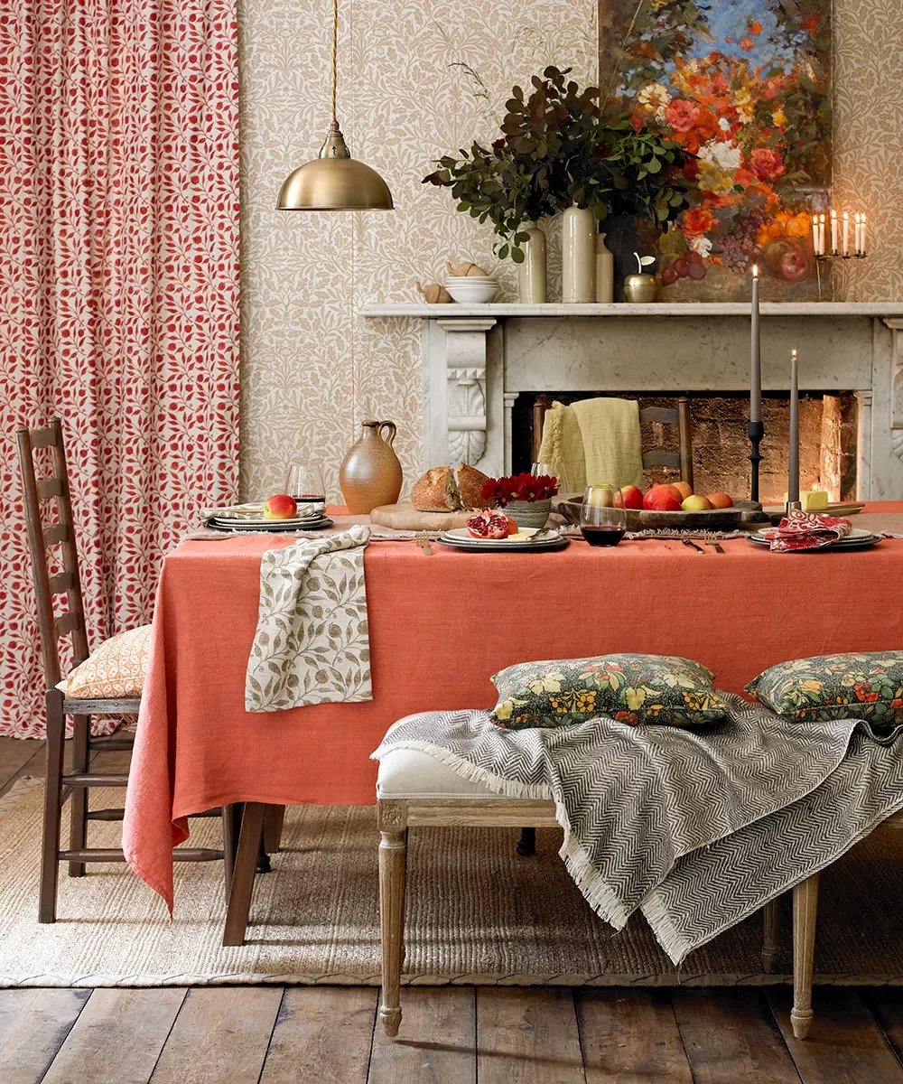 Dining room with a coral-draped table, botanical wallpaper, and marble fireplace.