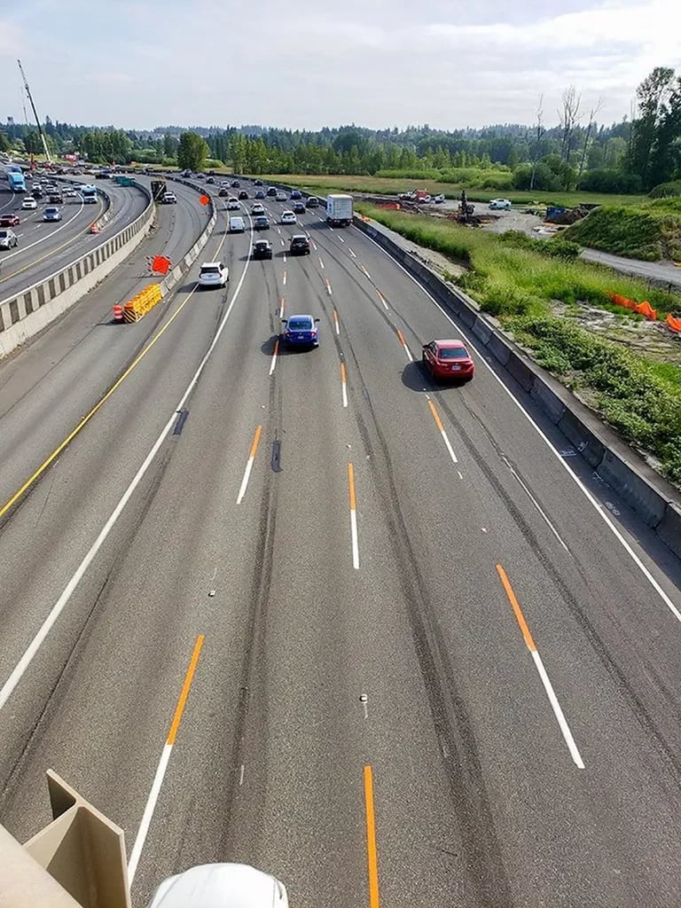  A view of a highway with cars driving down it. The highway is divided into multiple lanes, and there is a median separating the opposing directions of traffic.