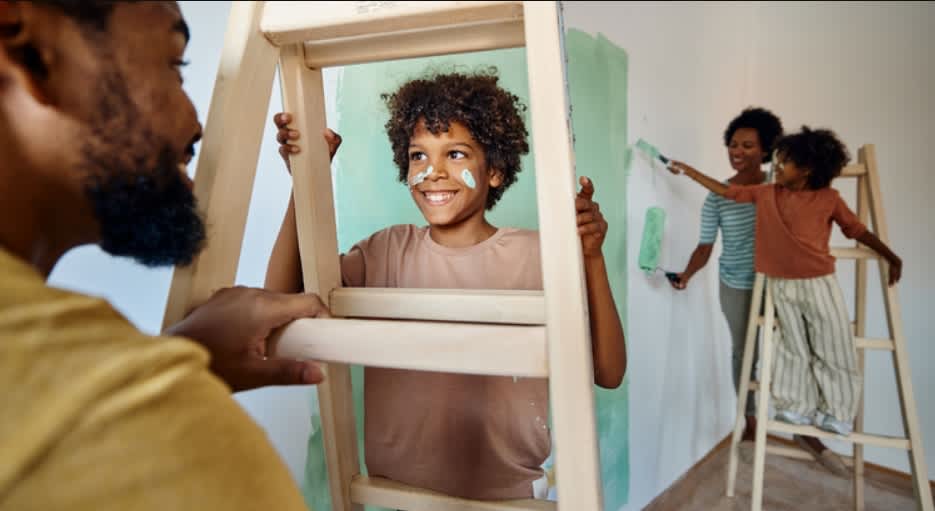 A man and woman are joyfully painting a child's room, surrounded by colorful paint cans and brushes.