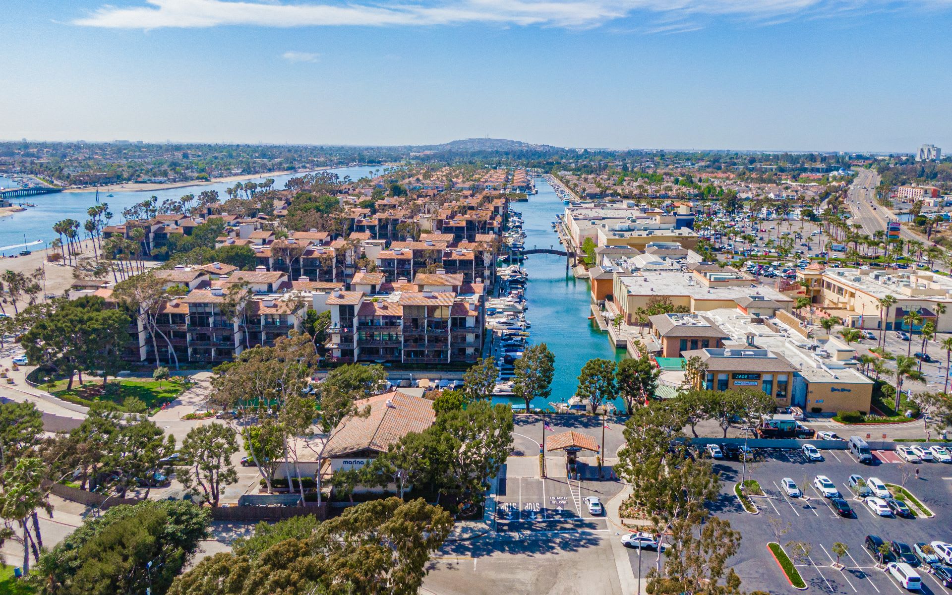 Aerial view of waterfront condos beside a boat-filled marina channel and palm-lined streets.