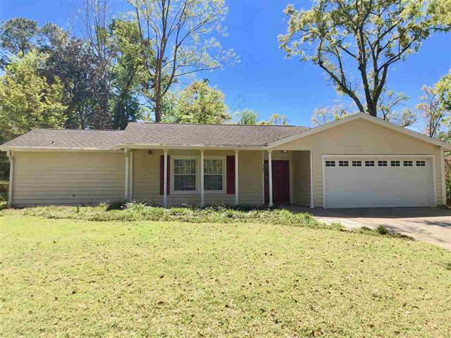 A single-story house in 261 Timberlane Rd with a simple design. The exterior appears to be a mix of brick and siding. The front yard is large but seems somewhat untended, with grass and a few trees.