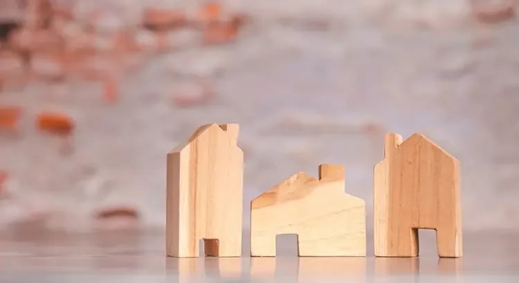 Small wooden house models placed on a surface, with a soft focus on the background. This image likely symbolizes real estate or home building.