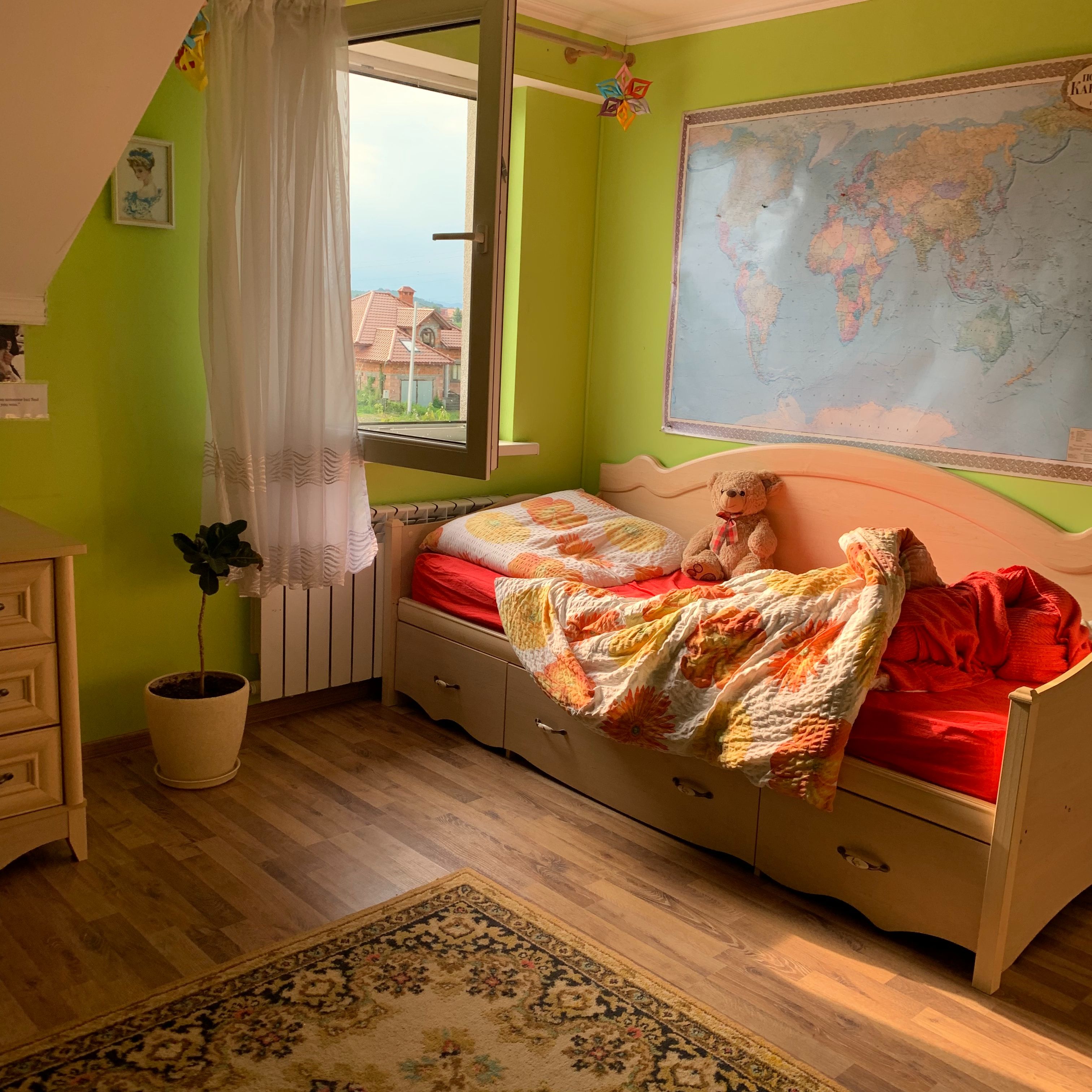 Child’s bedroom with bright green walls, a teddy bear on the bed, and a large world map.