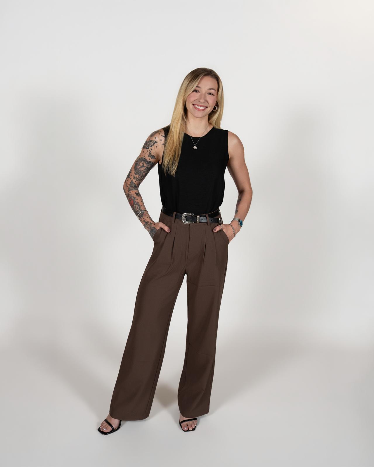 Kylie Rankin standing with her hands in her pockets, wearing a black top and brown trousers.