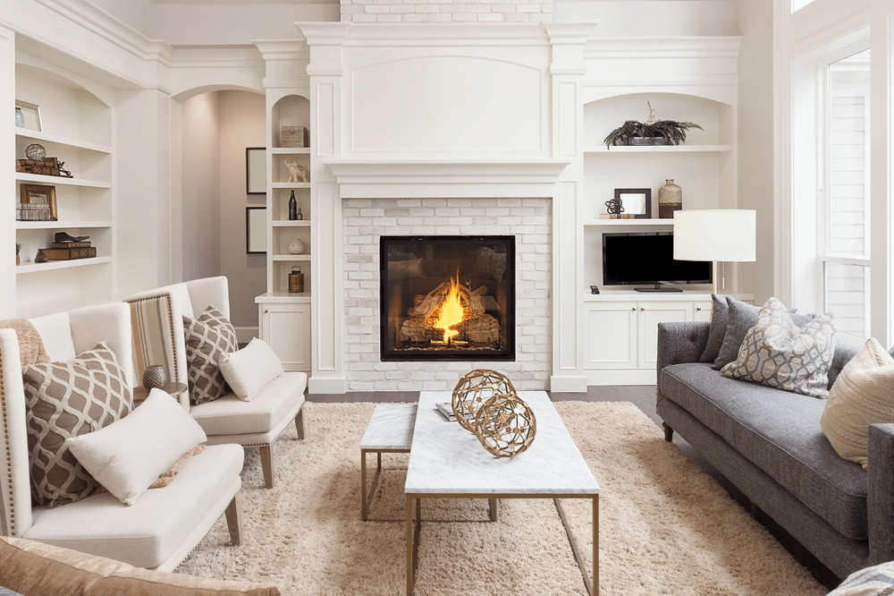Furnished living room with a lit white brick fireplace, built-ins, and sofas facing a marble coffee table.