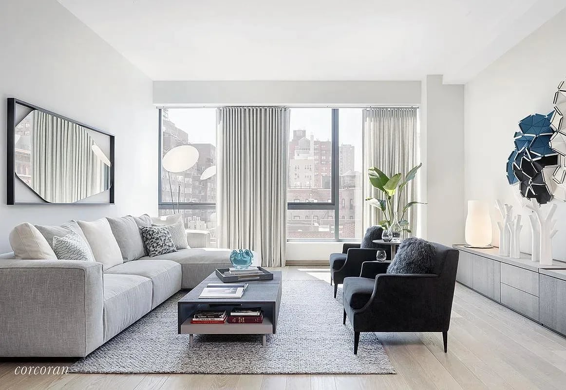 Bright living room with a gray sectional, dark armchairs, and city buildings visible through large windows.