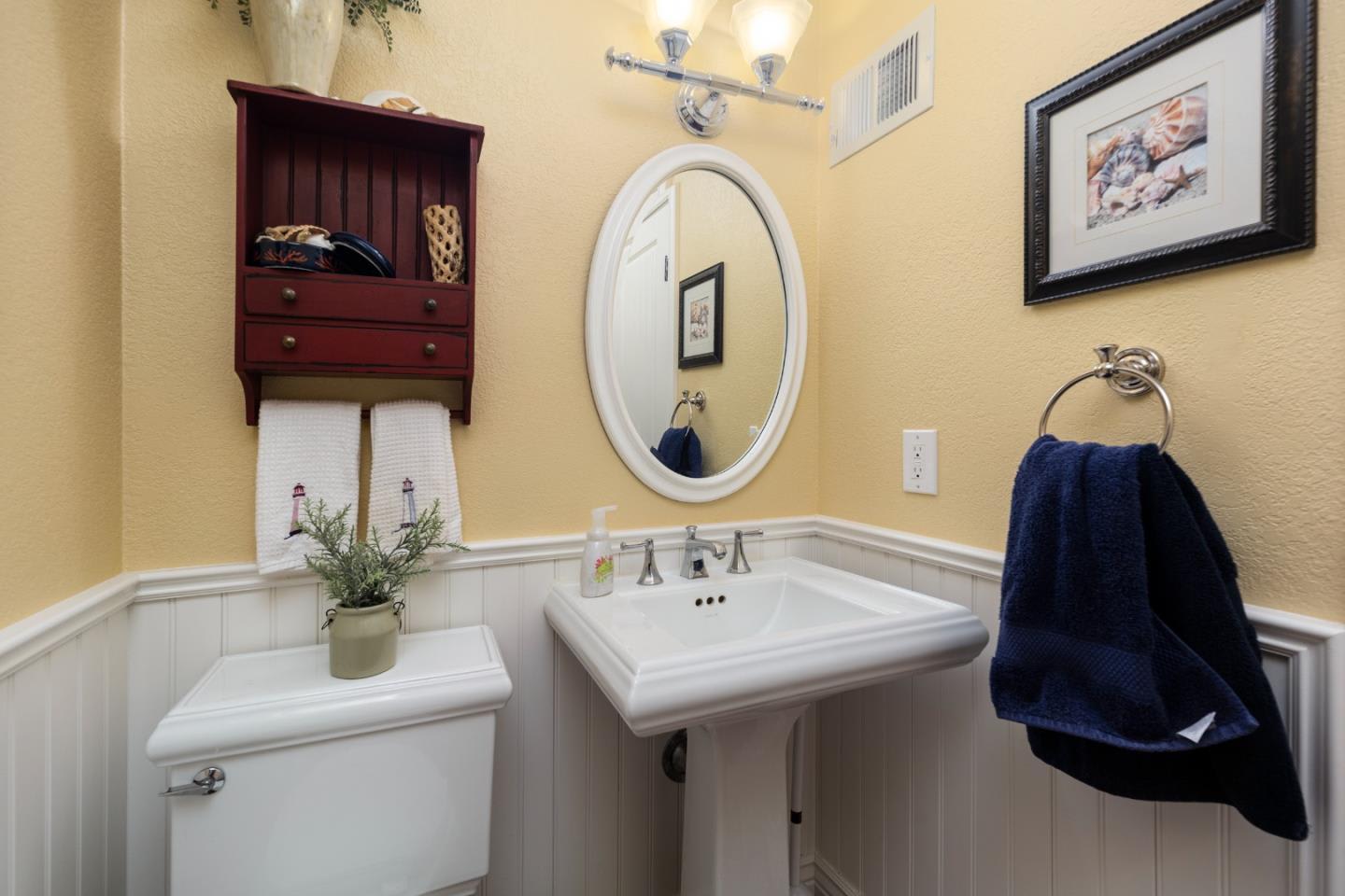 Bathroom with a pedestal sink, oval mirror, white wainscoting, and dark blue towels.
