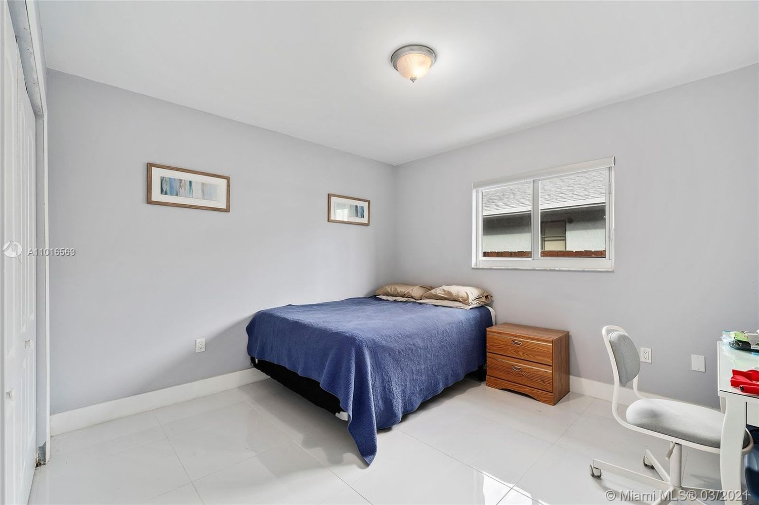 Bedroom with a blue-covered bed, wooden nightstand, white tile floor, and window.