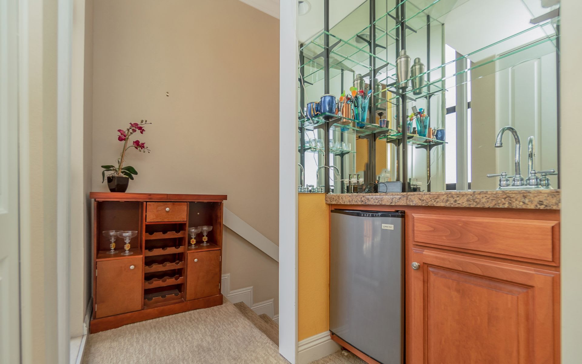 Wet bar with mirrored shelves, granite counter, beverage refrigerator, and wooden wine cabinet.
