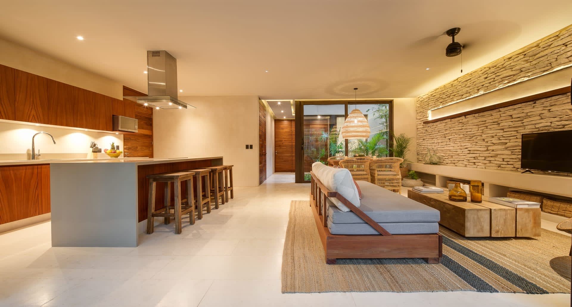 Open-plan condo living area with kitchen bar, stone accent wall, and sliding doors to a planted patio.